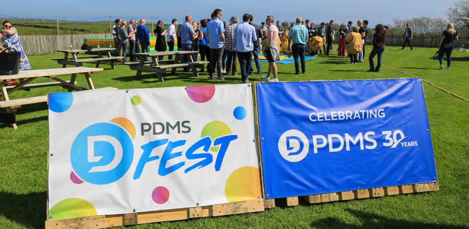 Banners reading PDMS Fest and the PDMS 30 years logo, with people socialising at a party outside in the background