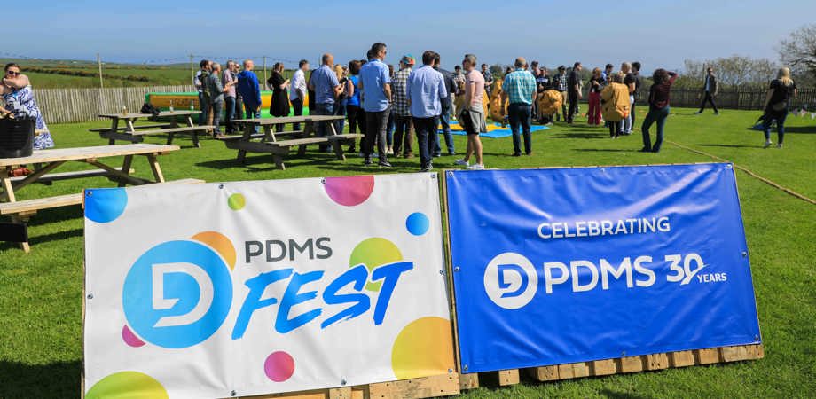 Banners reading PDMS Fest and the PDMS 30 years logo, with people socialising at a party outside in the background