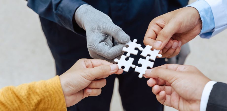 Four people each holding a jigsaw piece to fit together to represent collaboration between the government, the private sector and the public sector