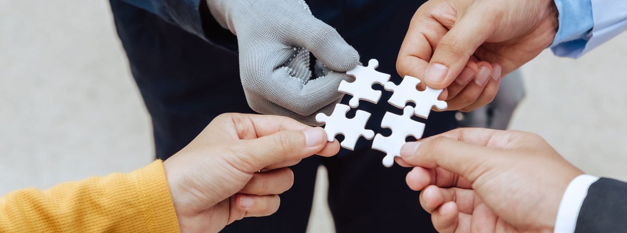 Four people each holding a jigsaw piece to fit together to represent collaboration between the government, the private sector and the public sector