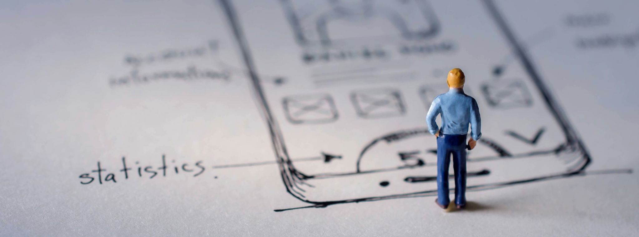 An image of hand-drawn UX design mock-ups with a mini figurine