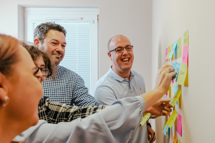 A photo of PDMS staff placing post-it notes on a wall as part of a UX workshop