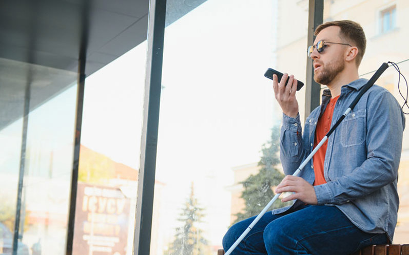 A photo of a blind man using AI accessibility tech on his phone while sat at a bus stop