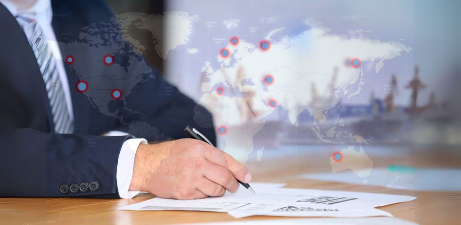 A businessman signing documents with a digital world map overlaid and a shipyard in the background