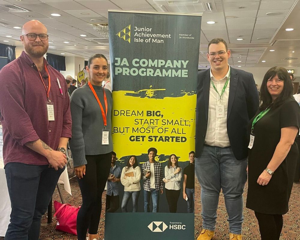 Four PDMS staff posing with a Junior Achievement banner