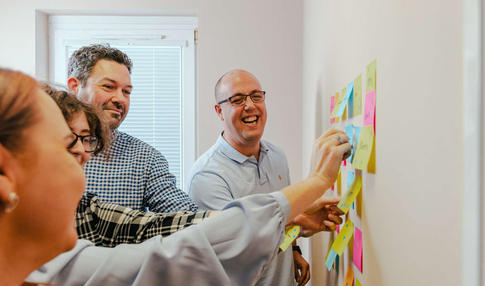 A group of people smiling and adding Post-It notes to a whiteboard