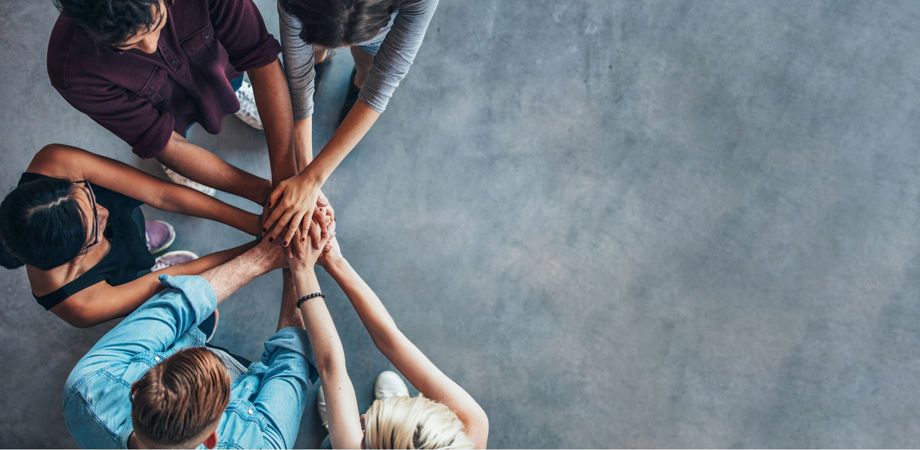 A photo from above of a diverse group of people with their hands reached out in a group high five