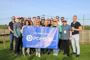 Twenty PDMS Scottish staff posing outside with a banner reading 'Celebrating PDMS 30 Years'