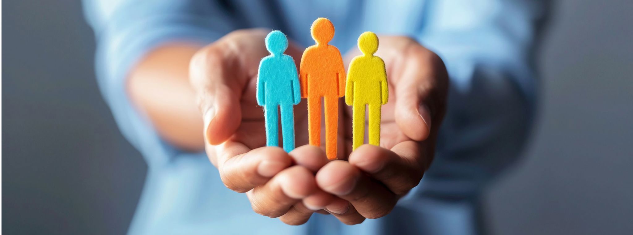 An image of a person holding a three felt people in blue, orange and yellow to represent employee wellbeing