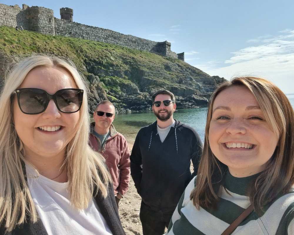 People smiling and standing on the beach with Peel Castle in the background