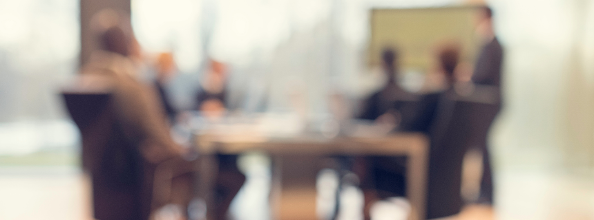 A blurred image of people sat at a board table
